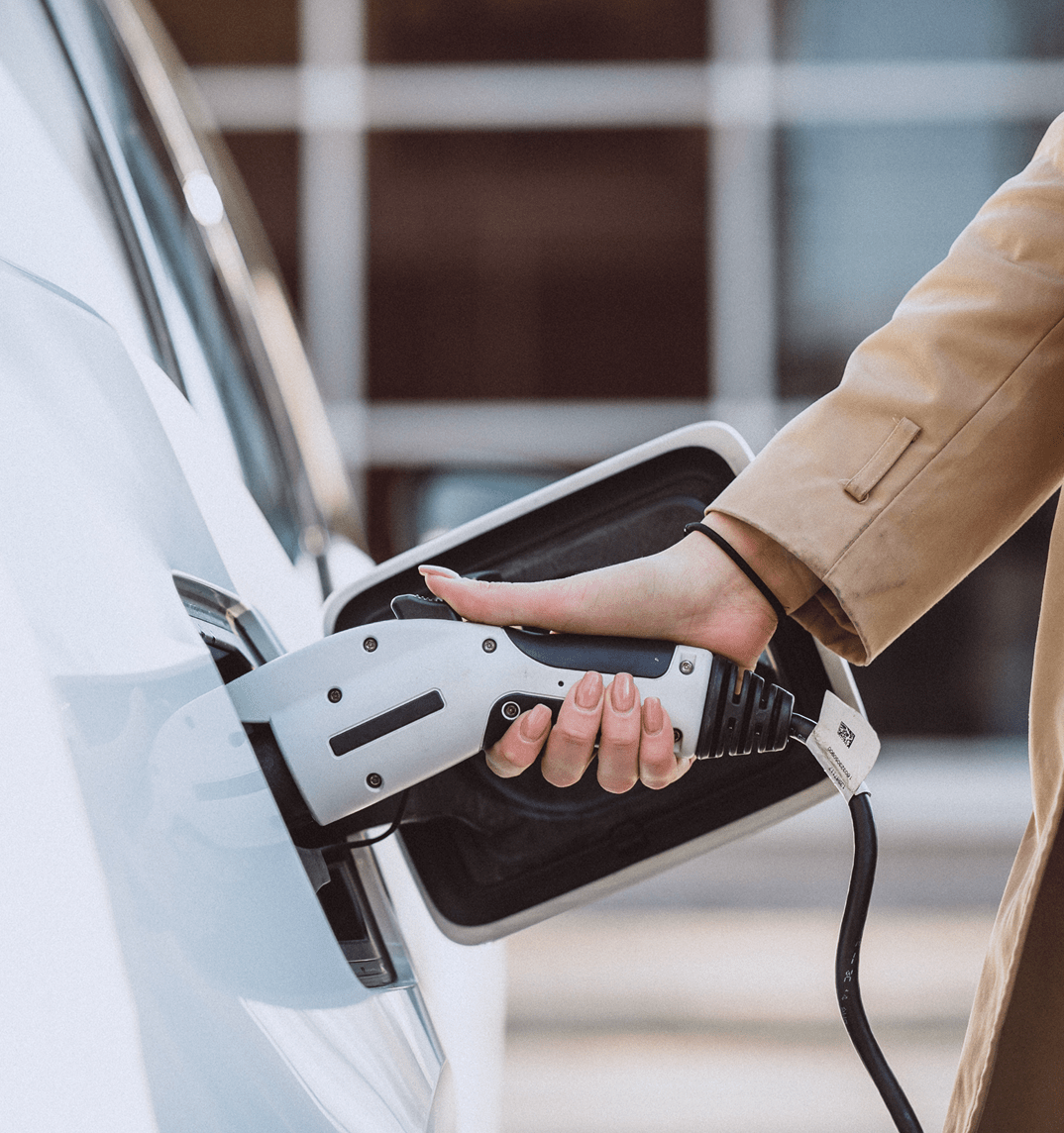 Electric Vehicle Charging Close-Up: Hand Plugging Charger into White Car